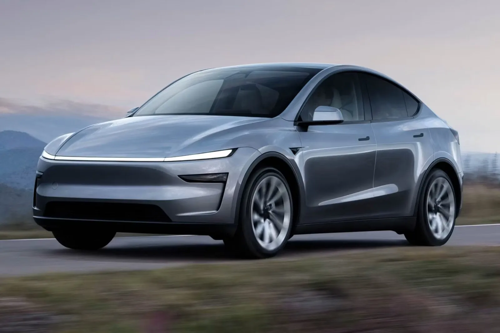 Tesla Model Y plateado circulando por una carretera de montaña al atardecer